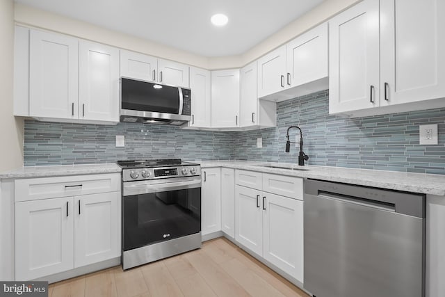 kitchen with appliances with stainless steel finishes, tasteful backsplash, sink, light hardwood / wood-style floors, and white cabinetry