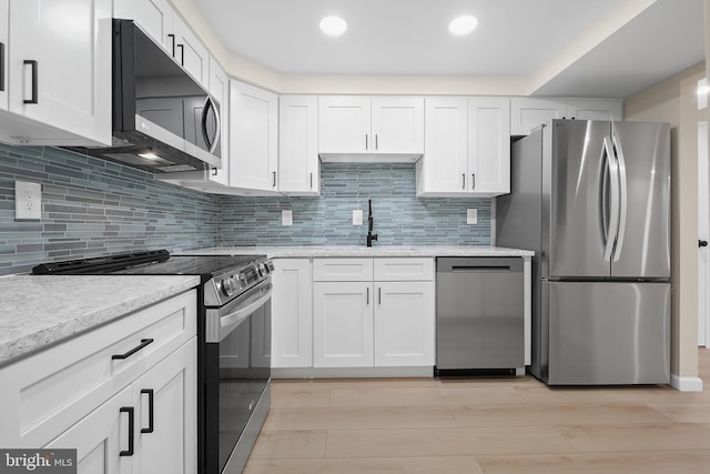 kitchen with white cabinets, appliances with stainless steel finishes, light hardwood / wood-style floors, and decorative backsplash