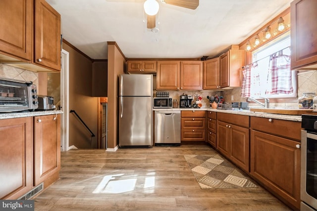 kitchen with stainless steel appliances, light stone counters, crown molding, light hardwood / wood-style floors, and decorative backsplash