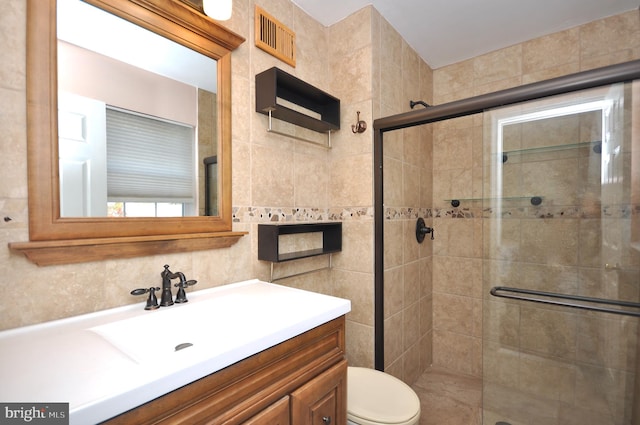 bathroom featuring vanity, toilet, a shower with door, and tile walls