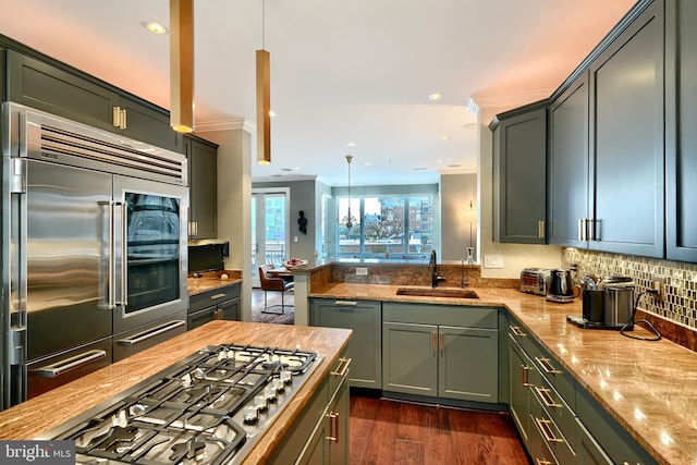 kitchen with dark wood-type flooring, sink, decorative light fixtures, appliances with stainless steel finishes, and kitchen peninsula