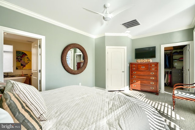 carpeted bedroom with a walk in closet, ensuite bath, ornamental molding, a closet, and ceiling fan