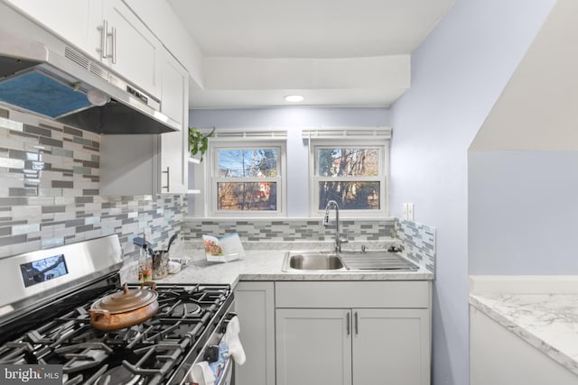 kitchen featuring decorative backsplash, white cabinets, stainless steel range with gas stovetop, a sink, and under cabinet range hood