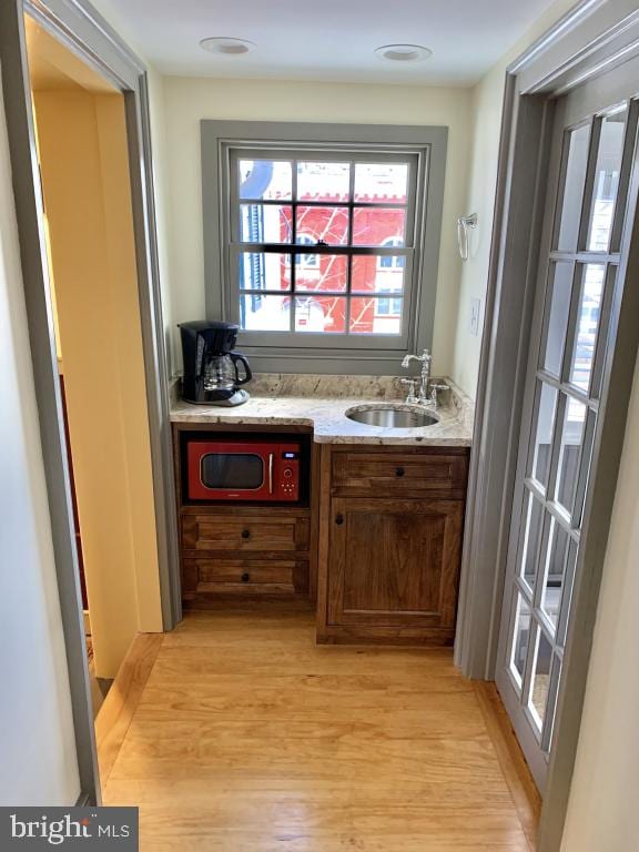 bar featuring light stone countertops, sink, and light hardwood / wood-style floors