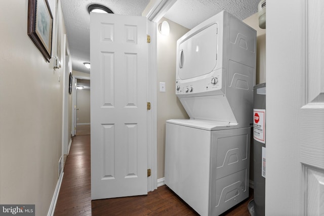 clothes washing area featuring a textured ceiling, stacked washer and dryer, dark wood-type flooring, and water heater