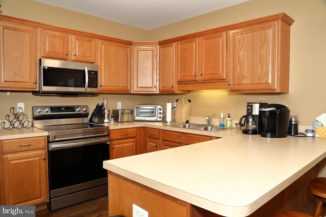 kitchen featuring sink, dark hardwood / wood-style flooring, kitchen peninsula, a breakfast bar, and appliances with stainless steel finishes