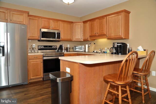 kitchen featuring a breakfast bar area, kitchen peninsula, dark hardwood / wood-style flooring, and stainless steel appliances