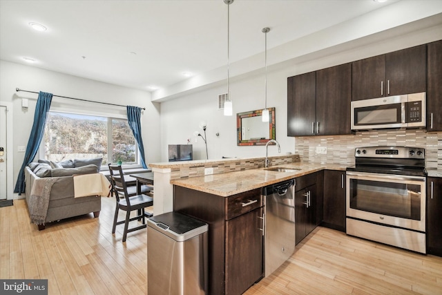 kitchen with dark brown cabinetry, hanging light fixtures, kitchen peninsula, light hardwood / wood-style floors, and appliances with stainless steel finishes