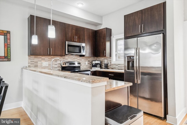 kitchen featuring light stone countertops, appliances with stainless steel finishes, kitchen peninsula, decorative light fixtures, and light hardwood / wood-style flooring