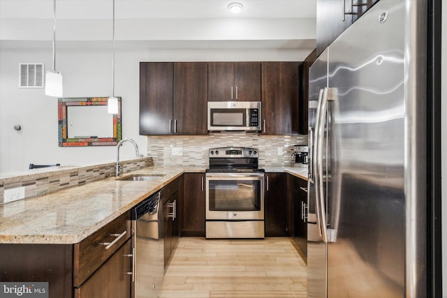 kitchen with sink, light wood-type flooring, decorative light fixtures, light stone counters, and stainless steel appliances