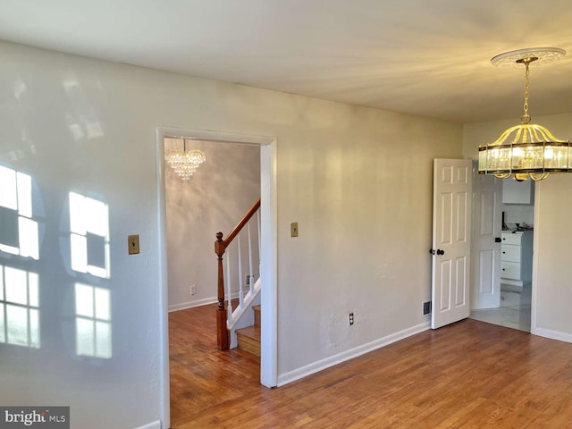 empty room featuring wood-type flooring and an inviting chandelier