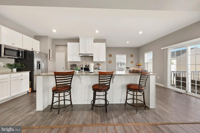 kitchen with white cabinets, appliances with stainless steel finishes, a kitchen island with sink, and a kitchen breakfast bar