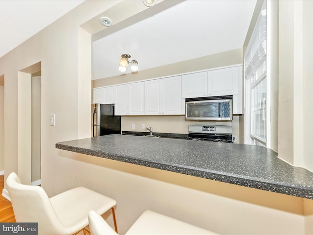 kitchen with kitchen peninsula, stainless steel appliances, sink, white cabinets, and hardwood / wood-style floors