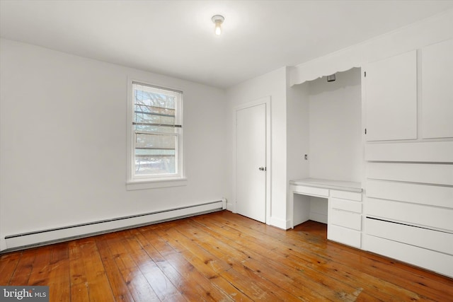 unfurnished bedroom with light hardwood / wood-style floors, built in desk, and a baseboard heating unit