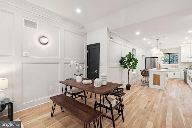 dining space with light hardwood / wood-style flooring, crown molding, and sink