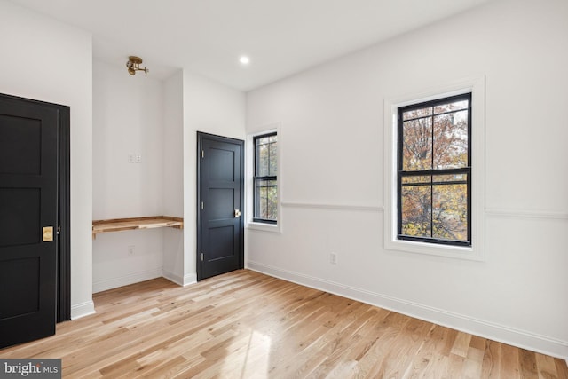 spare room with built in desk, light hardwood / wood-style floors, and a healthy amount of sunlight