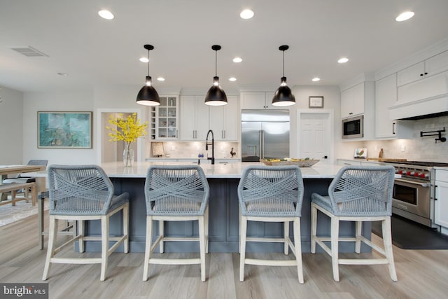 kitchen with white cabinets, a kitchen breakfast bar, a large island with sink, hanging light fixtures, and built in appliances