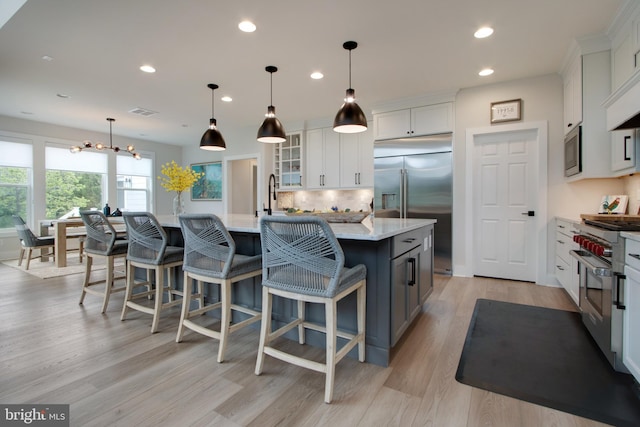 kitchen with built in appliances, light hardwood / wood-style flooring, hanging light fixtures, a large island with sink, and white cabinets