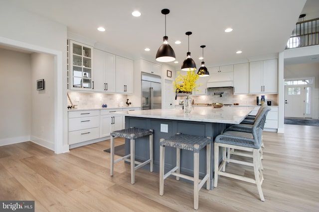 kitchen with a large island, pendant lighting, built in refrigerator, light hardwood / wood-style floors, and white cabinets