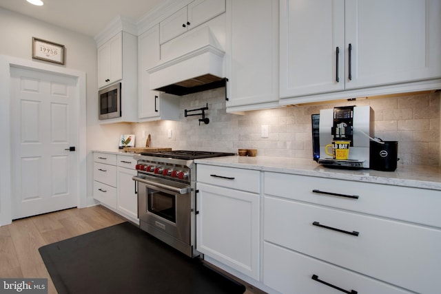 kitchen with built in microwave, white cabinetry, high end range, custom range hood, and light wood-type flooring