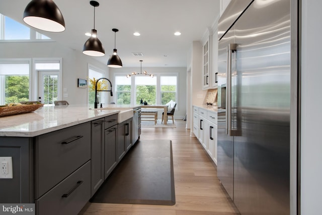 kitchen with sink, appliances with stainless steel finishes, white cabinetry, light stone counters, and an island with sink