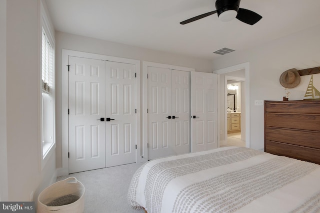 bedroom featuring ceiling fan, light colored carpet, and multiple closets