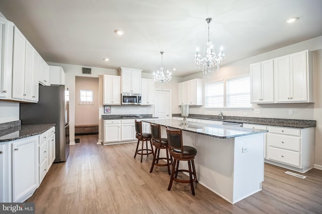 kitchen featuring stainless steel appliances, a center island with sink, white cabinets, light hardwood / wood-style floors, and hanging light fixtures