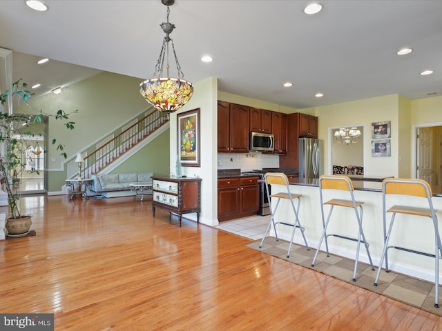 kitchen with hanging light fixtures, stainless steel appliances, tasteful backsplash, a kitchen bar, and light wood-type flooring