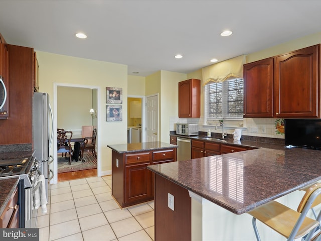 kitchen with appliances with stainless steel finishes, sink, a kitchen breakfast bar, decorative backsplash, and a center island