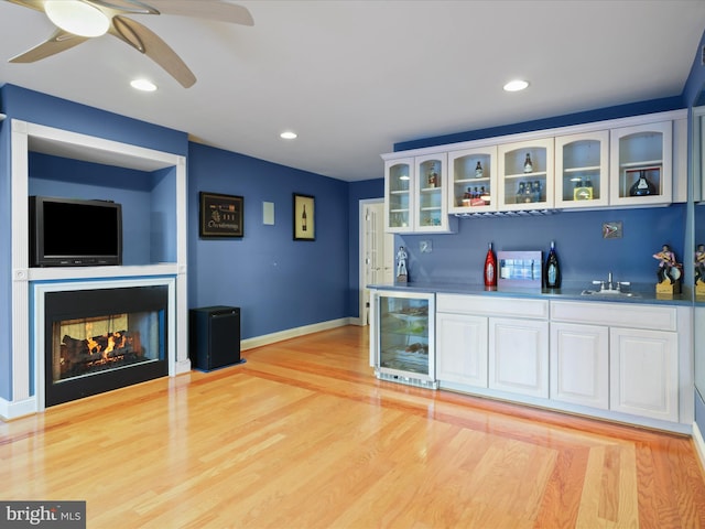 bar with a multi sided fireplace, beverage cooler, light hardwood / wood-style floors, and white cabinets