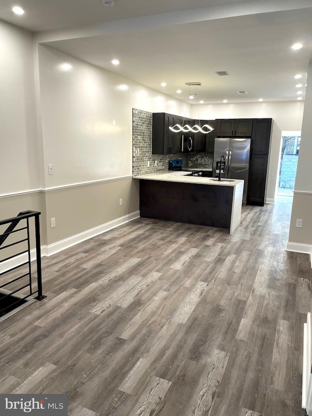 kitchen with kitchen peninsula, appliances with stainless steel finishes, backsplash, wood-type flooring, and hanging light fixtures