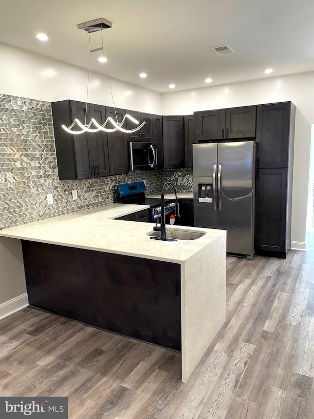 kitchen with kitchen peninsula, appliances with stainless steel finishes, backsplash, light wood-type flooring, and hanging light fixtures