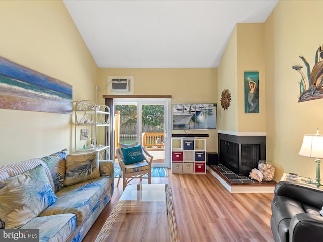 living room featuring a tile fireplace, hardwood / wood-style flooring, high vaulted ceiling, and a wall unit AC