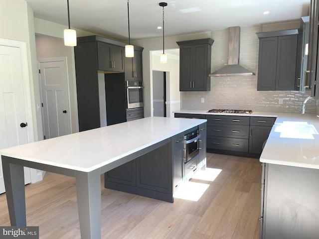 kitchen with sink, wall chimney exhaust hood, pendant lighting, and appliances with stainless steel finishes