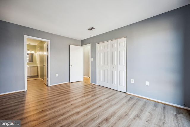 unfurnished bedroom with ensuite bath, a closet, and light wood-type flooring