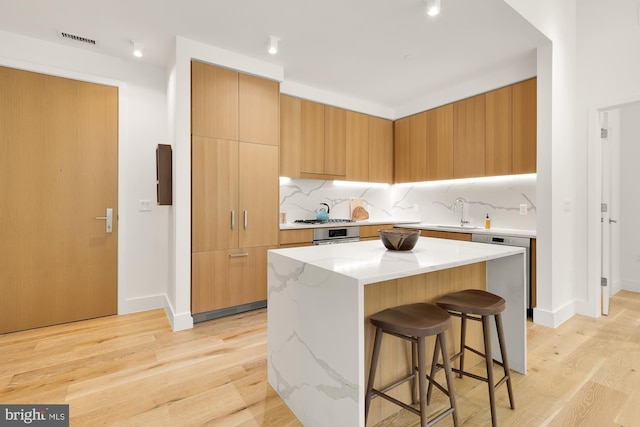 kitchen featuring a breakfast bar, decorative backsplash, light hardwood / wood-style floors, appliances with stainless steel finishes, and a kitchen island