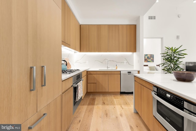 kitchen featuring light stone countertops, sink, light brown cabinets, stainless steel appliances, and light hardwood / wood-style floors