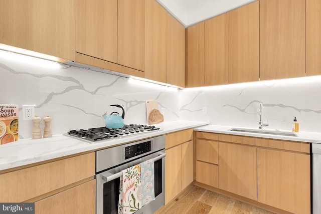 kitchen featuring backsplash, stainless steel appliances, sink, light brown cabinets, and light hardwood / wood-style flooring