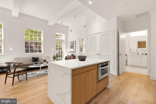 kitchen with beamed ceiling, a center island, light hardwood / wood-style floors, and stainless steel oven