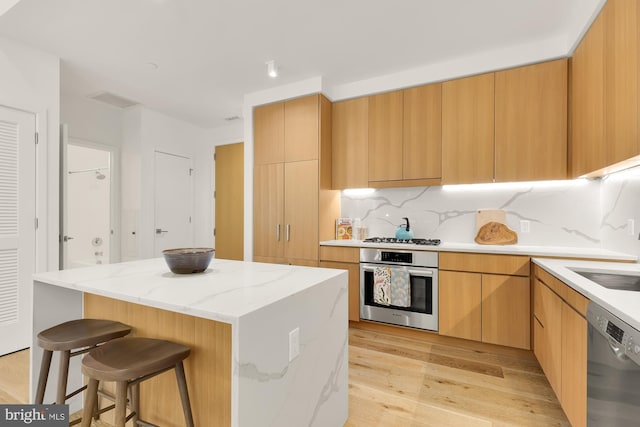 kitchen featuring a center island, light brown cabinets, decorative backsplash, appliances with stainless steel finishes, and light hardwood / wood-style floors