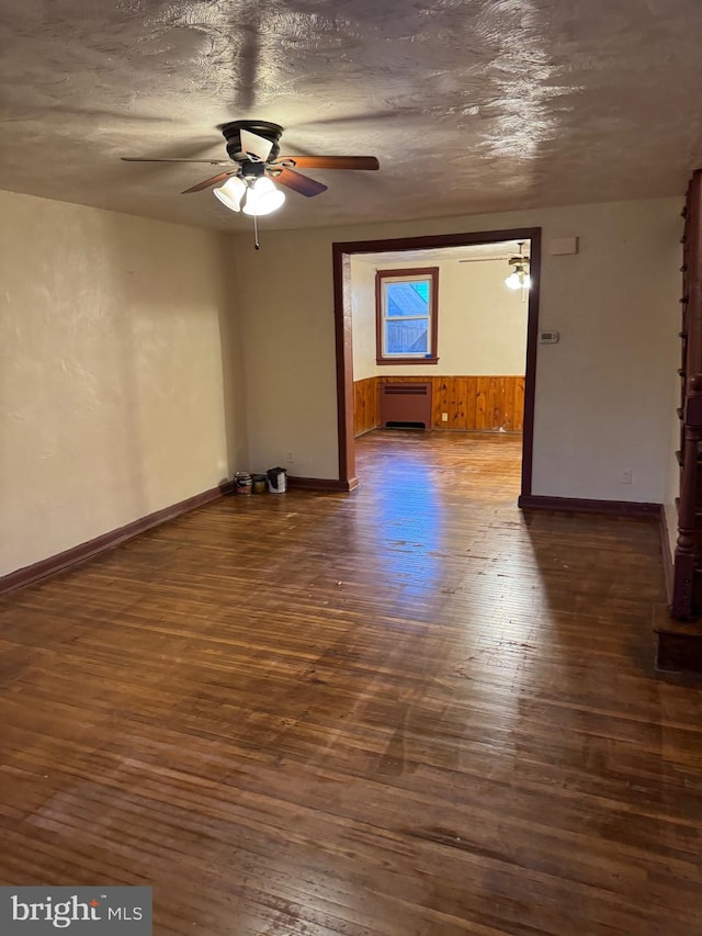 empty room featuring a textured ceiling, ceiling fan, wood walls, and dark wood-type flooring