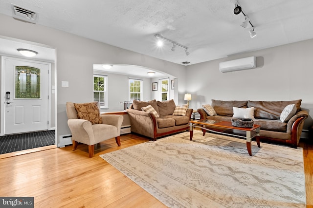 living room featuring light hardwood / wood-style flooring, a baseboard heating unit, a wall unit AC, a textured ceiling, and track lighting