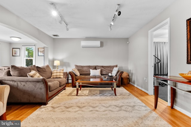 living room with baseboard heating, light hardwood / wood-style flooring, a wall mounted AC, and track lighting