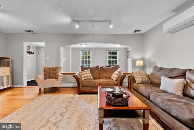 living room with baseboard heating, a wall unit AC, light hardwood / wood-style floors, and a textured ceiling