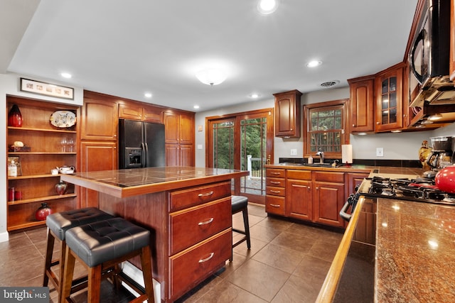 kitchen featuring a center island, black appliances, a kitchen breakfast bar, dark tile patterned flooring, and sink