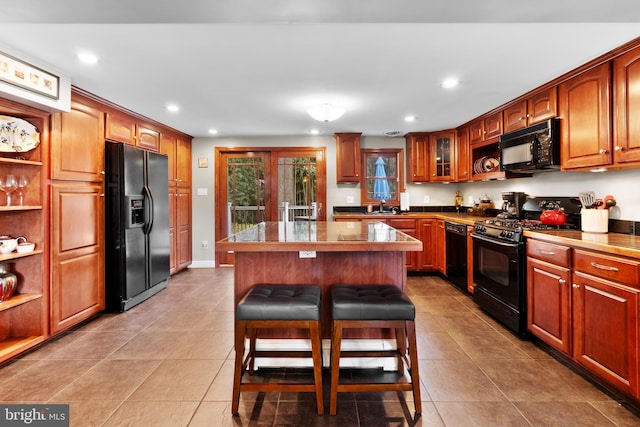 kitchen featuring a kitchen breakfast bar, a center island, light tile patterned flooring, and black appliances