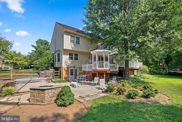 rear view of house featuring a patio area, a yard, a wooden deck, and a hot tub