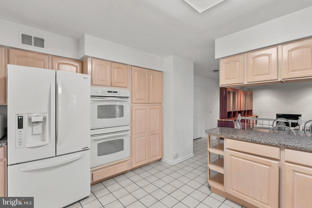 kitchen featuring light brown cabinets, white appliances, dark stone counters, and light tile patterned flooring