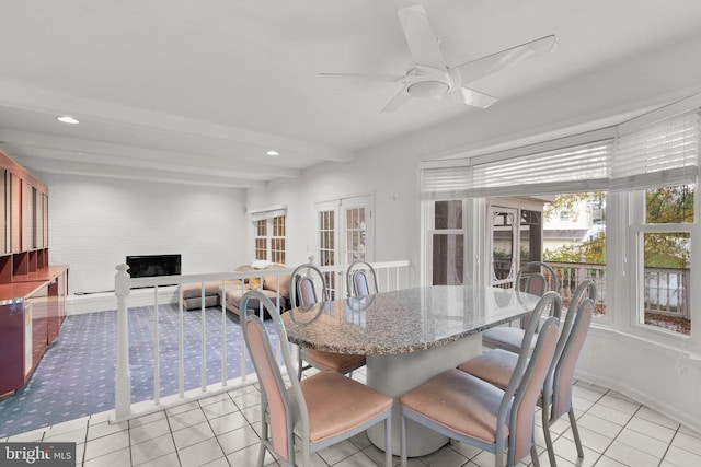 tiled dining area featuring ceiling fan, a large fireplace, beamed ceiling, and french doors