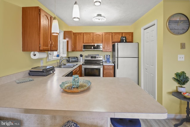 kitchen featuring sink, a textured ceiling, kitchen peninsula, pendant lighting, and stainless steel appliances